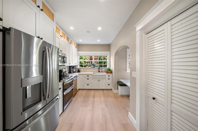 kitchen with light wood-type flooring, stainless steel appliances, arched walkways, white cabinets, and glass insert cabinets