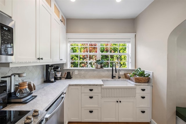 kitchen featuring stainless steel appliances, backsplash, a sink, arched walkways, and white cabinets