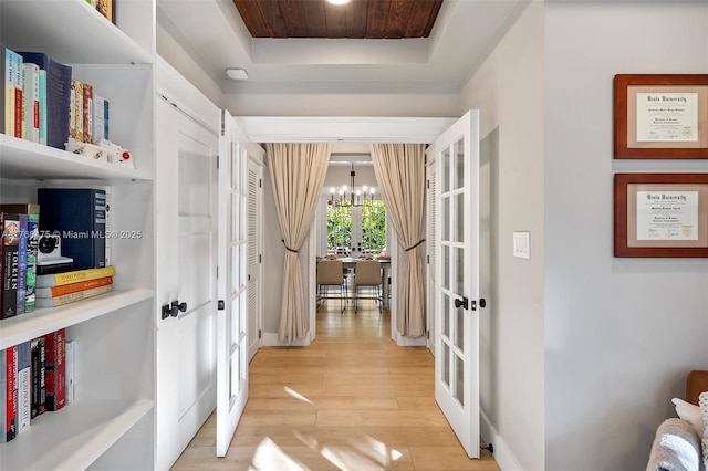 hallway featuring light wood-style floors, a raised ceiling, french doors, and a chandelier