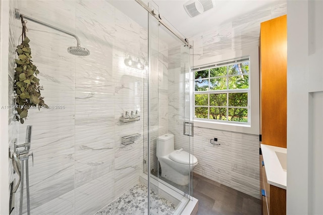 bathroom with vanity, tile walls, toilet, a shower stall, and visible vents