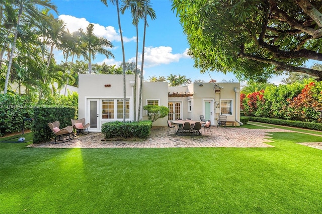 rear view of property with stucco siding, a lawn, french doors, and a patio area