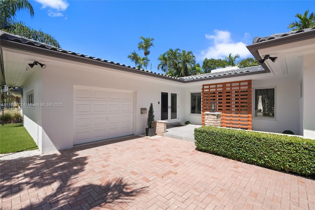 1221 NE 87th St, Miami, FL 33138 - view of front of home featuring a garage, decorative driveway, stucco siding, french doors, and a tiled roof