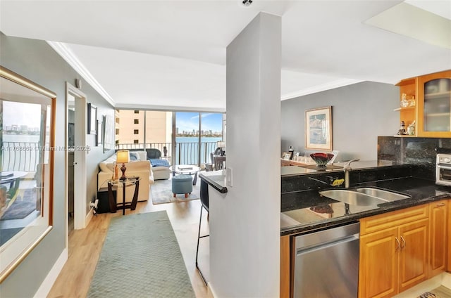 kitchen featuring ornamental molding, dark stone counters, a sink, light wood-style floors, and glass insert cabinets