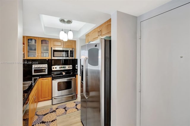 kitchen with stainless steel appliances, backsplash, a raised ceiling, dark countertops, and glass insert cabinets