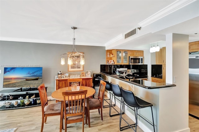 dining area featuring an inviting chandelier, light wood-style flooring, ornamental molding, and visible vents