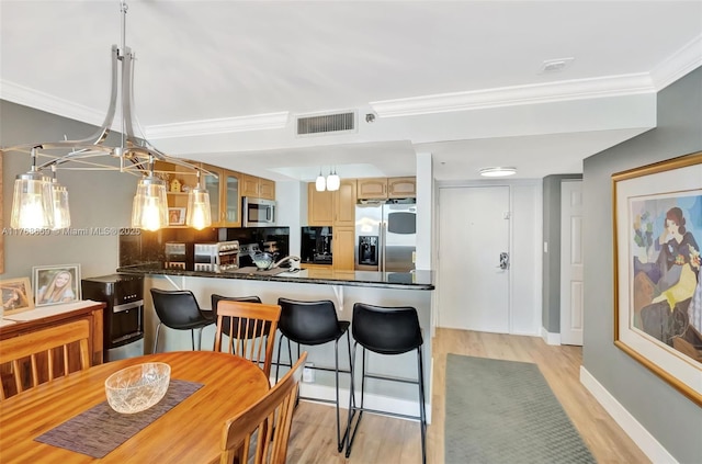 kitchen with dark countertops, stainless steel appliances, visible vents, light wood-style floors, and ornamental molding