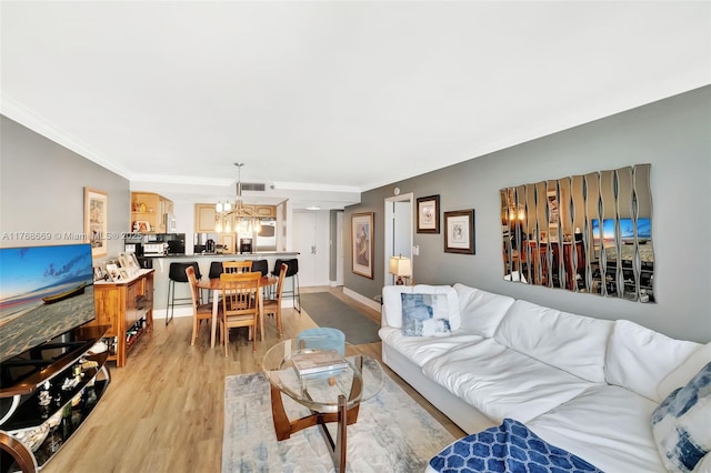 living room featuring ornamental molding, baseboards, a chandelier, light wood-style floors, and visible vents