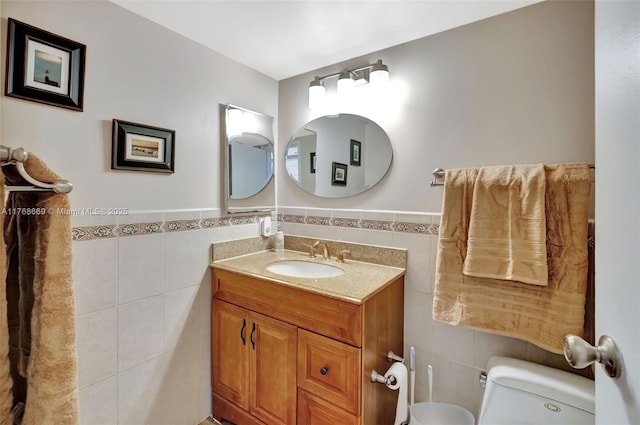 bathroom featuring toilet, vanity, a wainscoted wall, and tile walls