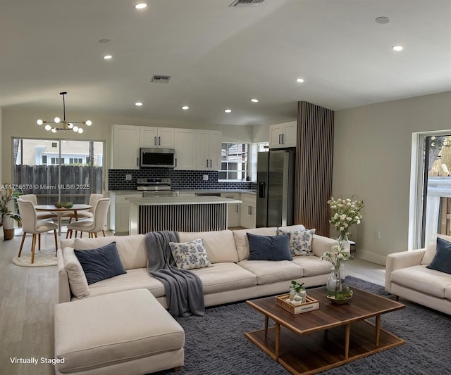 living room with visible vents, a healthy amount of sunlight, a chandelier, and wood finished floors