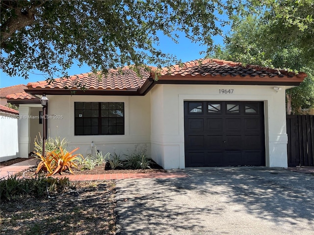 mediterranean / spanish house with a tile roof, concrete driveway, stucco siding, fence, and an attached garage