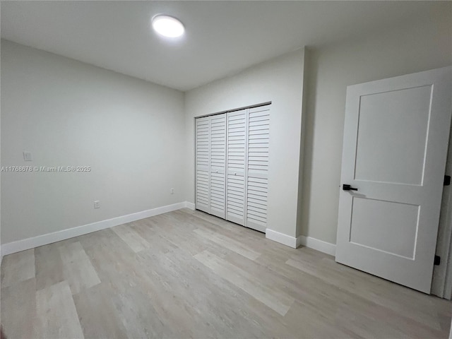 unfurnished bedroom with light wood finished floors, baseboards, and a closet