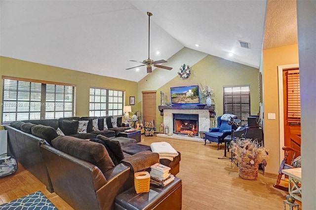 living room featuring visible vents, high vaulted ceiling, a lit fireplace, ceiling fan, and light wood-type flooring