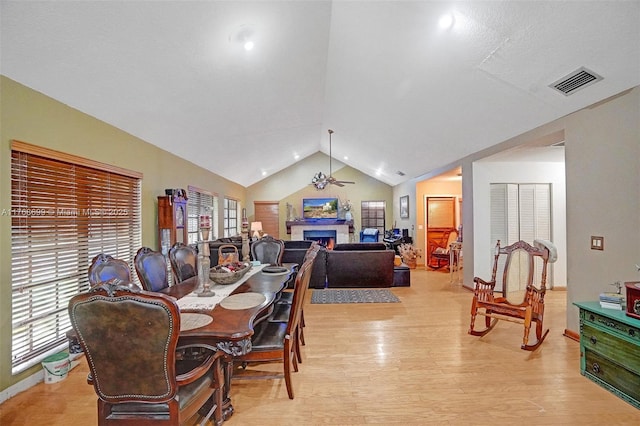 dining space with visible vents, light wood-style flooring, a lit fireplace, lofted ceiling, and ceiling fan
