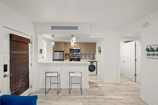 740 Meridian Ave Unit 11, Miami Beach, FL 33139 - kitchen with stainless steel appliances, washer / dryer, light wood-style flooring, tasteful backsplash, and light countertops