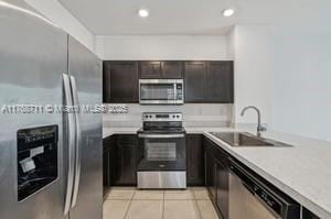 kitchen featuring light tile patterned flooring, light countertops, dark brown cabinetry, a sink, and stainless steel appliances