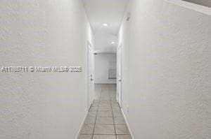 corridor with baseboards, a textured wall, and tile patterned floors