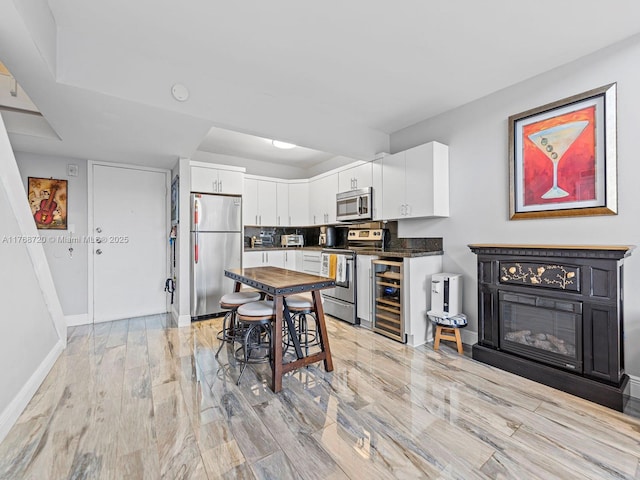 820 NW 87th Ave Unit 409, Miami, FL 33172 - kitchen featuring light wood finished floors, baseboards, beverage cooler, white cabinets, and stainless steel appliances