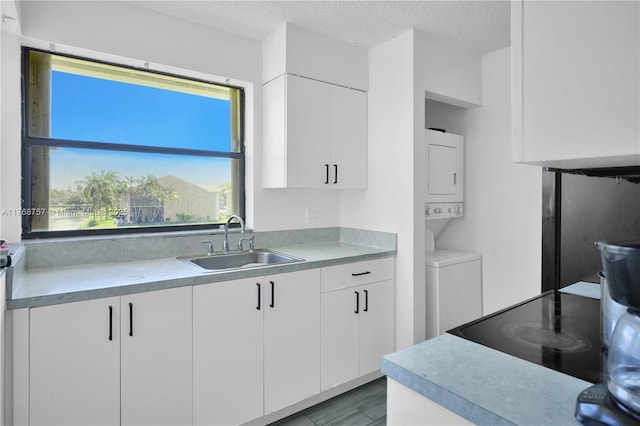 kitchen featuring stacked washer and dryer, light countertops, white cabinets, a sink, and a textured ceiling
