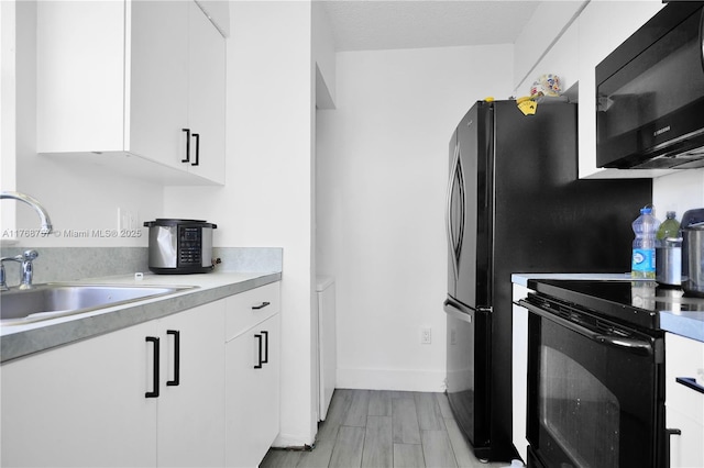 kitchen featuring light countertops, white cabinets, black appliances, a sink, and baseboards