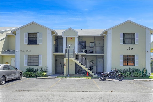 view of front of home with stucco siding, stairs, and uncovered parking