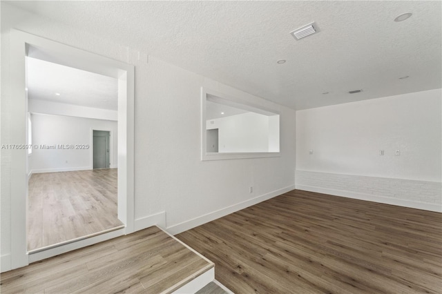 empty room with visible vents, a textured ceiling, baseboards, and wood finished floors