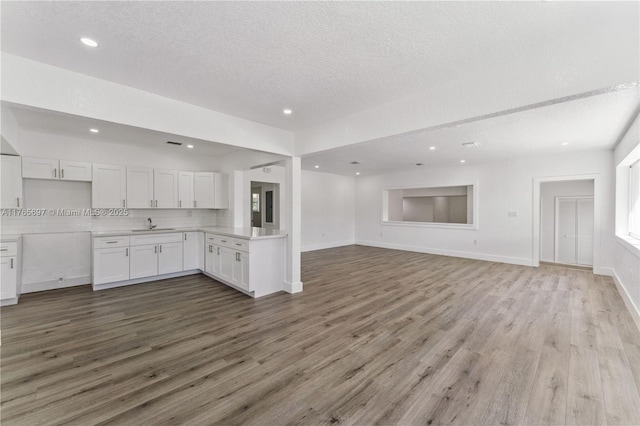 kitchen featuring wood finished floors, open floor plan, white cabinets, decorative backsplash, and recessed lighting