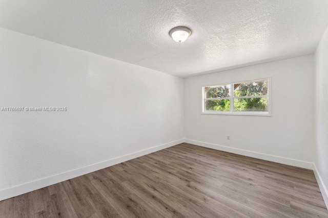 empty room with baseboards, wood finished floors, and a textured ceiling