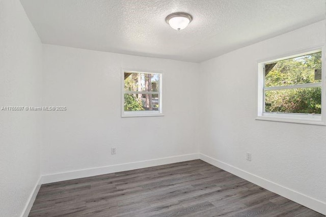 spare room featuring dark wood-type flooring, a textured ceiling, and baseboards