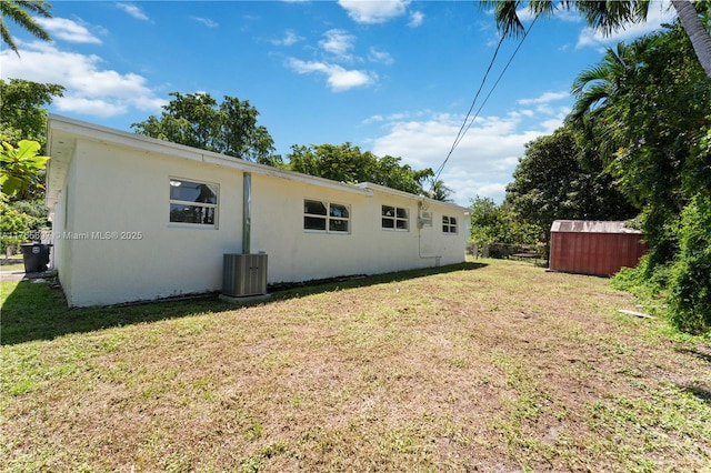 back of property featuring stucco siding, fence, central AC, and a yard