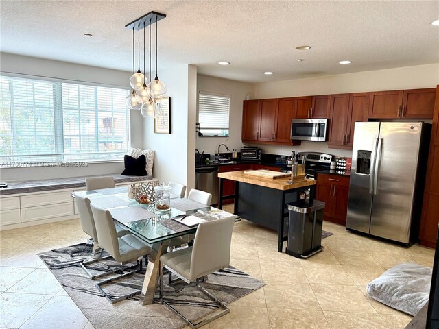 kitchen with decorative light fixtures, butcher block countertops, appliances with stainless steel finishes, a textured ceiling, and a sink