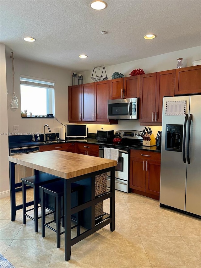 kitchen featuring recessed lighting, a sink, appliances with stainless steel finishes, a textured ceiling, and a kitchen bar