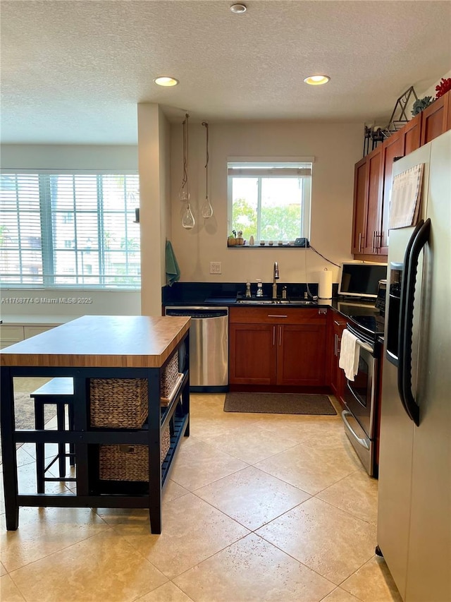 kitchen featuring brown cabinetry, a sink, appliances with stainless steel finishes, a textured ceiling, and dark countertops