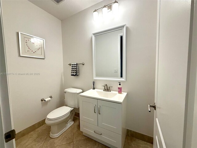 half bathroom with baseboards, toilet, vanity, and tile patterned flooring