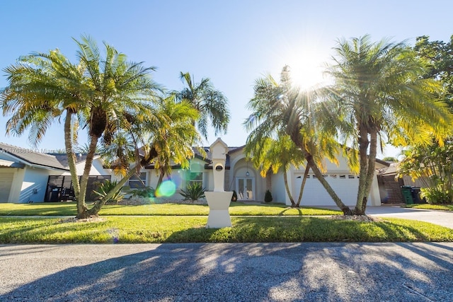 view of property hidden behind natural elements with driveway, a garage, a front lawn, and stucco siding