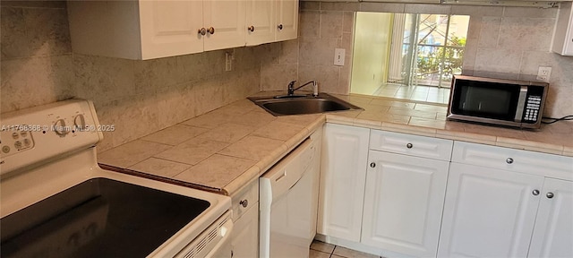 kitchen featuring white appliances, tile countertops, a sink, white cabinets, and backsplash