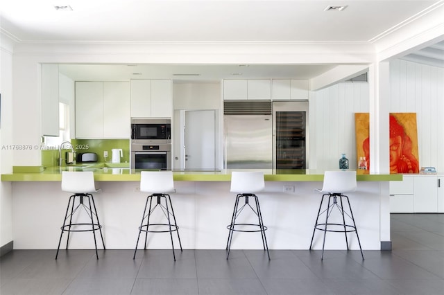 kitchen with modern cabinets, built in appliances, white cabinets, and a breakfast bar