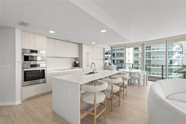 kitchen with double oven, light wood-type flooring, a sink, visible vents, and modern cabinets