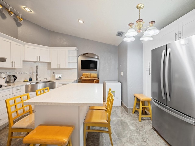 kitchen featuring visible vents, light countertops, freestanding refrigerator, and arched walkways
