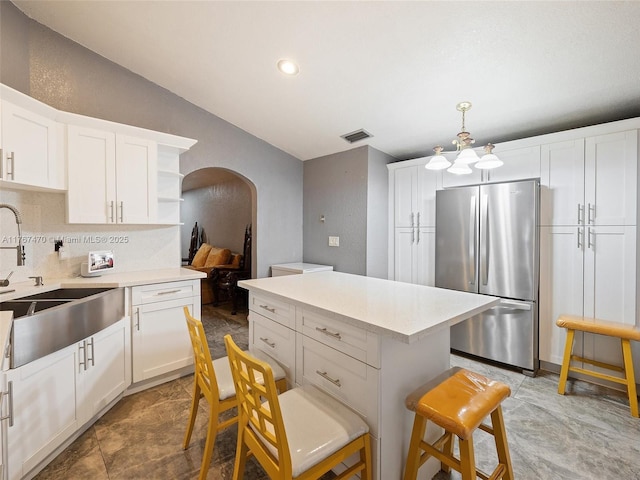 kitchen featuring light countertops, visible vents, a sink, arched walkways, and freestanding refrigerator