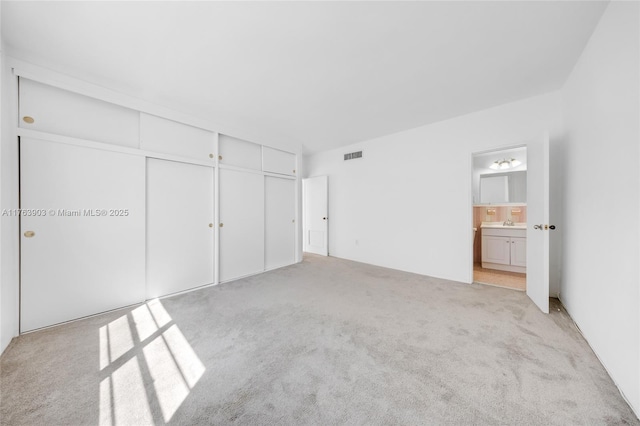 unfurnished bedroom with light carpet, ensuite bathroom, visible vents, and a closet