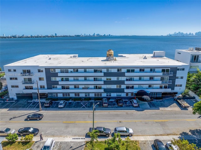 view of building exterior with uncovered parking, a water view, and a view of city