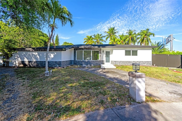 view of front of house featuring stucco siding, stone siding, a front lawn, and fence