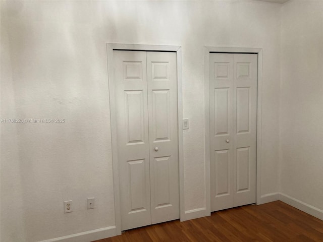 5450 NW 107th Ave Unit 705, Doral, FL 33178 - unfurnished bedroom featuring baseboards, dark wood-style flooring, and two closets