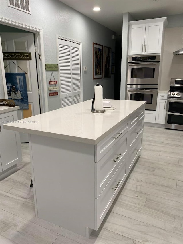 kitchen featuring visible vents, a center island, white cabinetry, stainless steel appliances, and light countertops