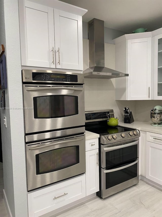 kitchen with light countertops, white cabinets, wall chimney exhaust hood, and appliances with stainless steel finishes