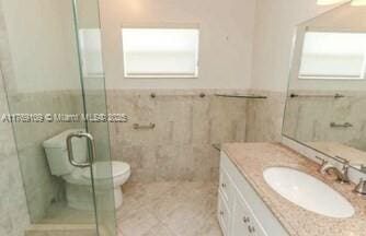 full bath featuring toilet, vanity, tile walls, wainscoting, and a stall shower