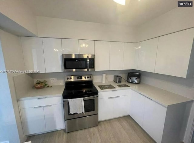 kitchen with white cabinets, stainless steel appliances, light countertops, modern cabinets, and light wood-style flooring