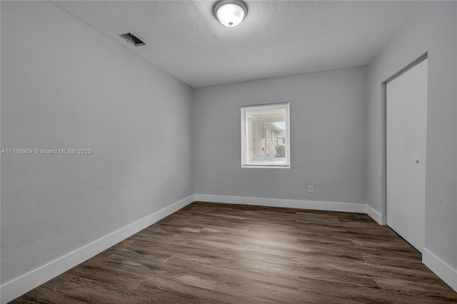 spare room featuring dark wood-style flooring, visible vents, baseboards, and a textured ceiling