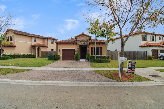 mediterranean / spanish house with a front yard, a tile roof, fence, stucco siding, and decorative driveway