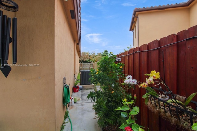 view of side of property with a patio, central AC unit, a fenced backyard, and stucco siding